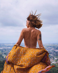 Woman removing dress while standing against sky