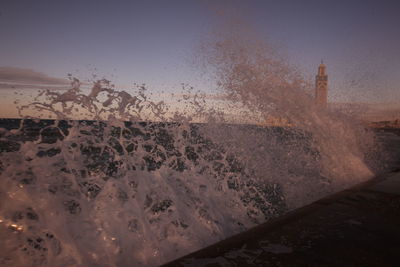 Waves flowing at sea with mosque hassan ii in background against sky