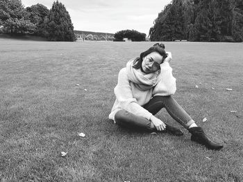 Portrait of smiling woman sitting on field against sky