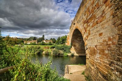 Arch bridge over river against cloudy sky