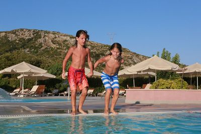 Boys jumping in swimming pool against clear sky