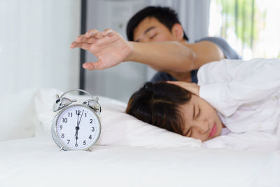 Man reaching alarm clock with woman on bed at home
