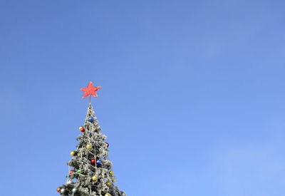 Christmas tree decorated with christmas balls and red star outdoors on blue sky background.