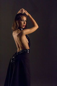 Young woman wearing backless dress while posing against black background