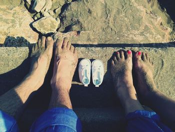 Low section of couple sitting with baby booties at beach