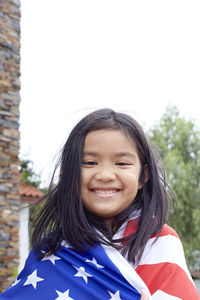 Portrait of smiling girl wearing american flag against sky