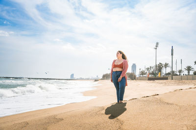 Woman standing at beach against cloudy sky