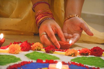 Midsection of woman putting diya by rangoli during festival