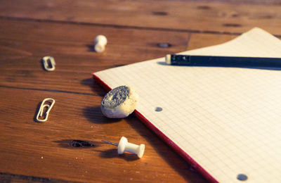 High angle view of book with pencil and rubber by pins on wooden table