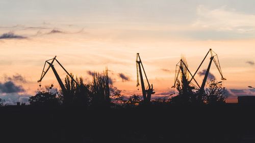 Silhouette cranes against sky during sunset