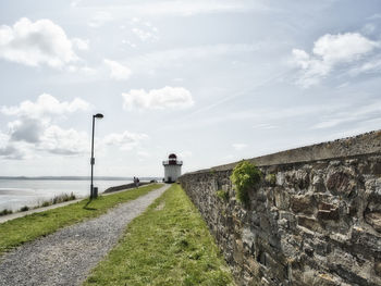 Footpath by wall against sky