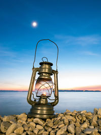 Close-up of illuminated light by sea against blue sky