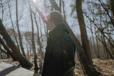 A guy in profile stands in the forest, a bright sunny day, looks to the side, enjoys nature