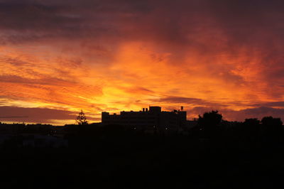 Silhouette houses against dramatic sky during sunset