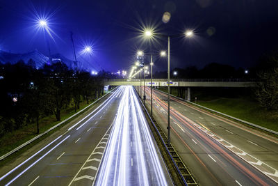 Light trails on illuminated city against sky at night