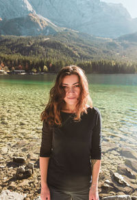A smiling girl in a black sweater stands against the backdrop of a mountain lake eibsee, german alps