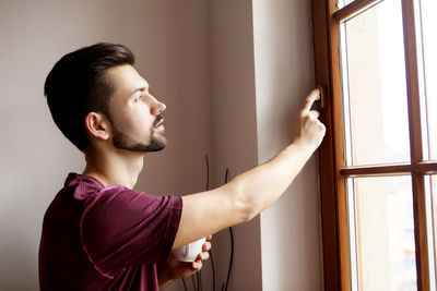 Young man looking through window at home