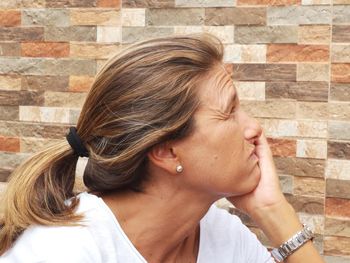 Side view of woman with hand on chin sitting against wall