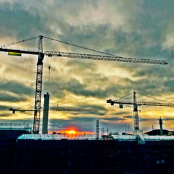 Silhouette cranes against cloudy sky at sunset
