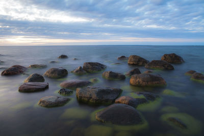 Scenic view of rocks at sea shore against sky