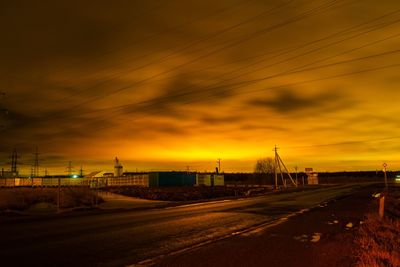 Road by buildings against sky during sunset