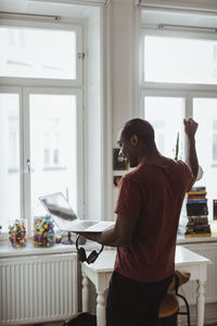 Successful male entrepreneur holding laptop and headphones with raised fist at home office