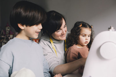 Smiling mother with son and daughter looking at sewing machine