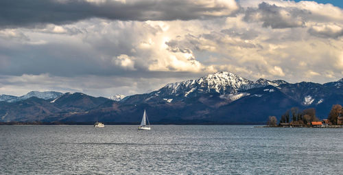 Sailboats sailing on sea by mountains against sky