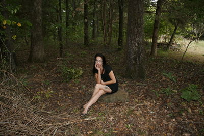 Portrait of young woman sitting on land in forest