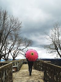 Rear view of woman with pink umbrella standing against sky during rainy season