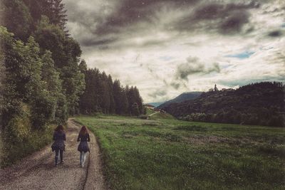 Rear view of woman standing on landscape against cloudy sky