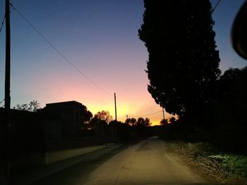 Road by silhouette trees against clear sky during sunset