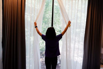 Rear view of woman standing by window at home