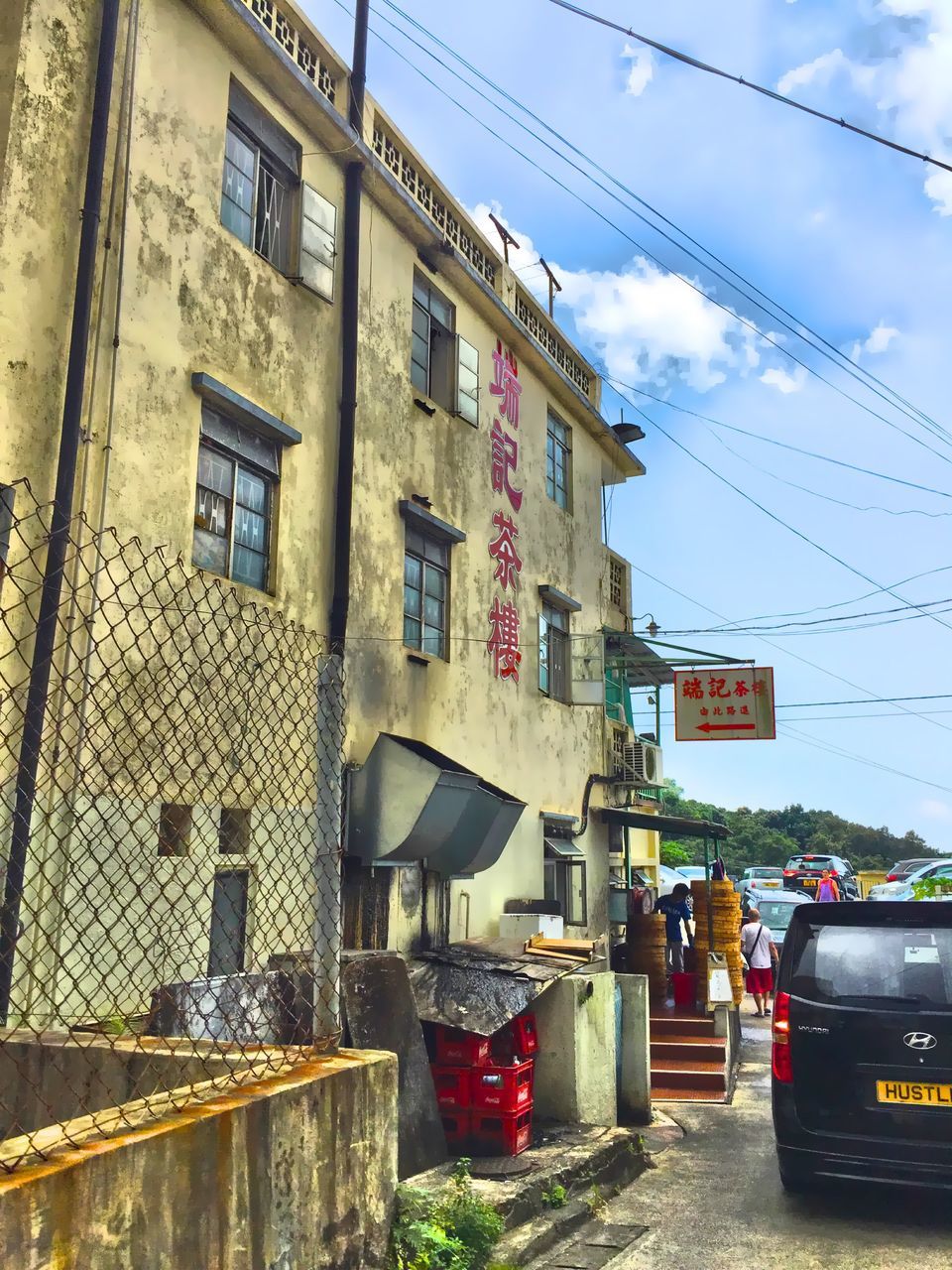 architecture, building exterior, built structure, street, transportation, power line, sky, low angle view, cable, city, car, land vehicle, road, residential building, building, residential structure, incidental people, day, mode of transport, outdoors