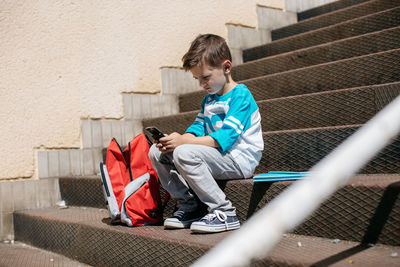 Full length of boy using on mobile phone while sitting on steps