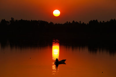 Silhouette person in lake against sky during sunset