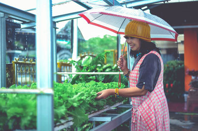 Rear view of woman with umbrella standing in greenhouse