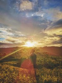 Rear view of man standing on landscape against sky during sunset