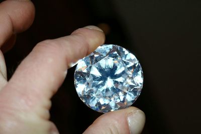 Close-up of hand holding diamond against black background