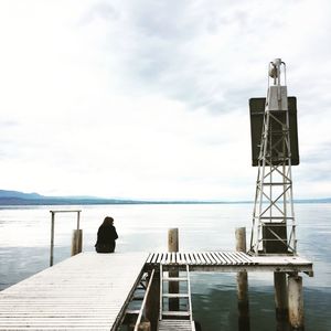 Man sitting on pier at sea against sky