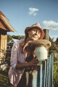 Woman with eyes closed leaning on jar full of milk by fence