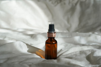 Cosmetic amber glass bottle with essential oil on white bed background with sunlights