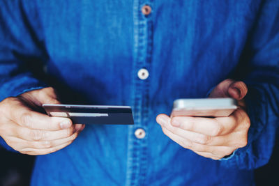 Midsection of man using mobile phone while holding credit card