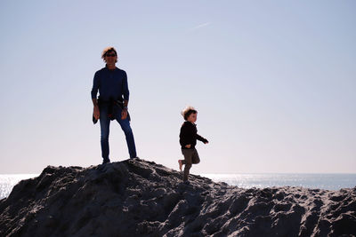 Father and son on rock formation at beach against clear sky