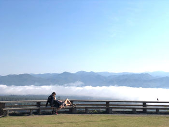 People sitting on bench looking at mountains against sky