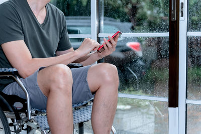 Midsection of man using mobile phone while sitting by window