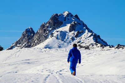 Rear view of man skiing on snowcapped mountain against clear blue sky