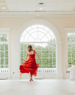 Full length of beautiful woman standing by window at home