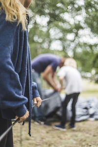 Midsection of teenage girl assisting family in pitching tent at campsite