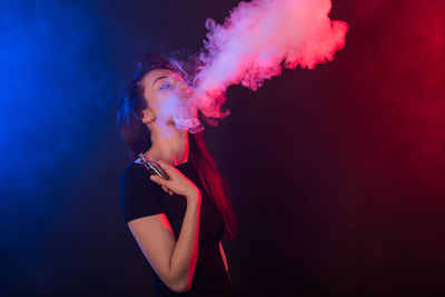 Young woman smoking against black background